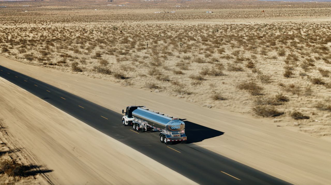 An aerial view of a tanker truck traveling down an empty road in a desert landscape.